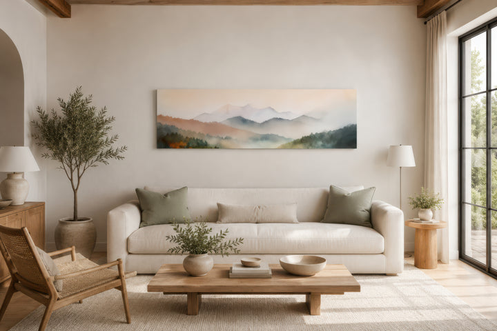 A wide canvas print of a pink and green pastel mountain landscape hangs above a white sofa.