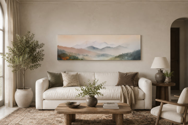 A wide canvas print of a pastel pink and green mountain landscape hangs above a white sofa.