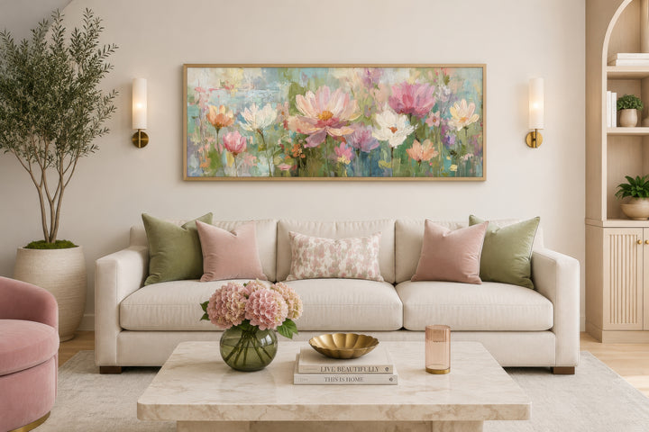A long horizontal botanical painting featuring pink and green flowers in a gold frame above a sofa.