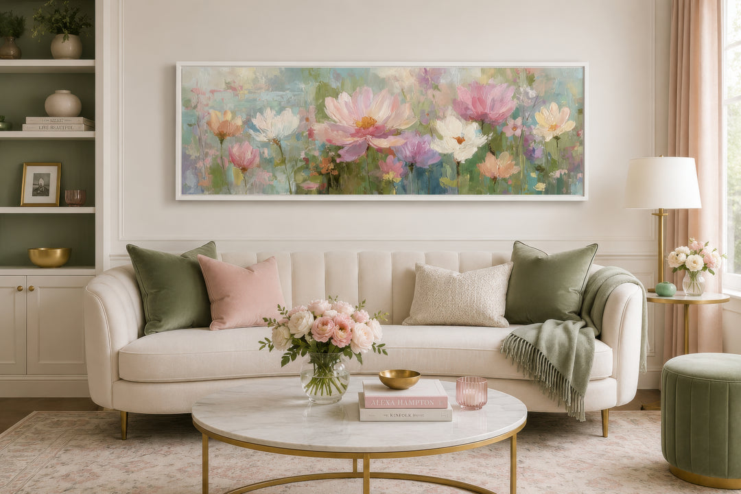 A long horizontal canvas painting of pink and white flowers in a white frame above a cream sofa.