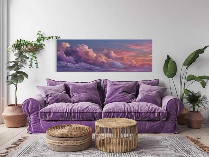 Panoramic canvas wall art of pink and purple sunset clouds hanging above a purple velvet sofa.