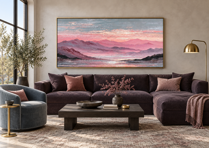 Large horizontal pink mountain landscape canvas print in a gold frame above a dark velvet sofa.