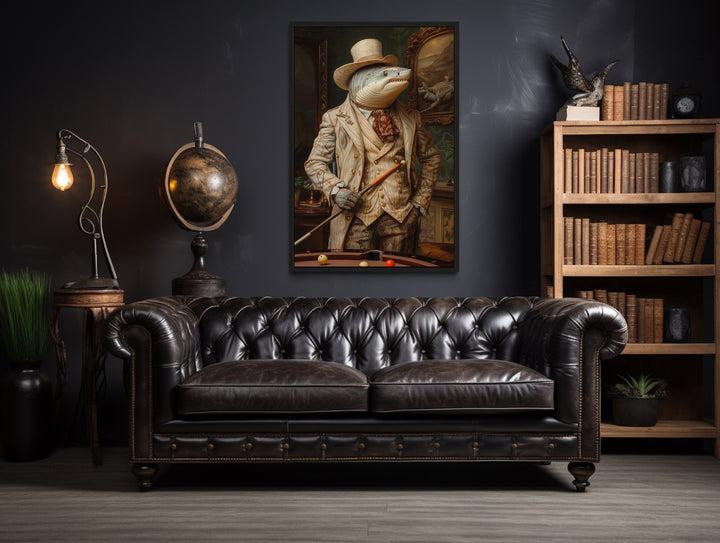 Framed canvas art of a shark in a suit holding a pool cue, hanging above a black leather sofa.