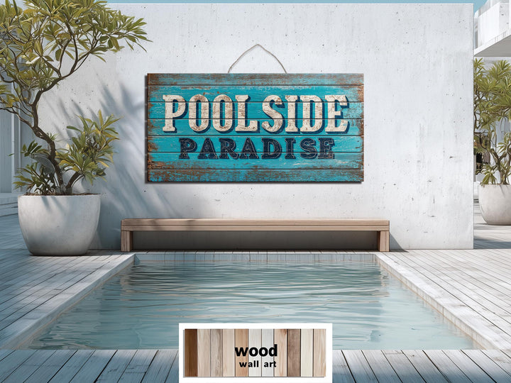 A rustic wood wall art sign reading Poolside Paradise hangs on a white wall above a swimming pool.