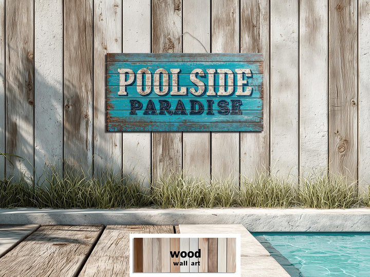 A rustic blue Poolside Paradise sign on a weathered wood wall above a pool deck.