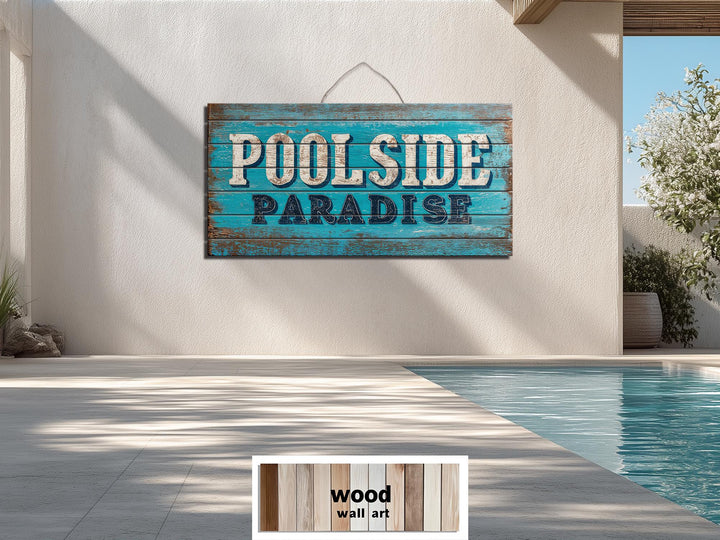 A rustic wood wall art sign reading Poolside Paradise hangs on a wall above a swimming pool.