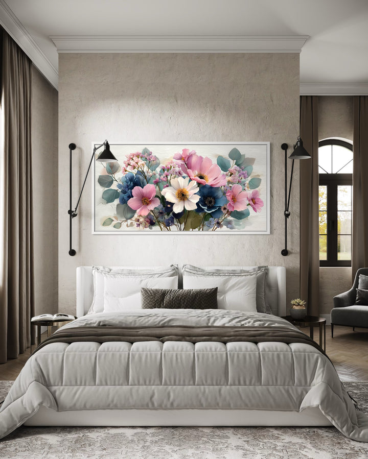 Pretty blue and pink wildflower bouquet framed canvas wall art hanging above a bed in a bedroom.