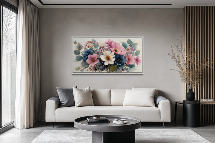 Horizontal framed canvas wall art of a blue and pink wildflower bouquet above a modern sofa.