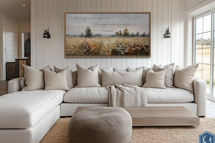 Psalm 18:19 scripture wall art on a wildflower field canvas above a neutral sectional sofa.