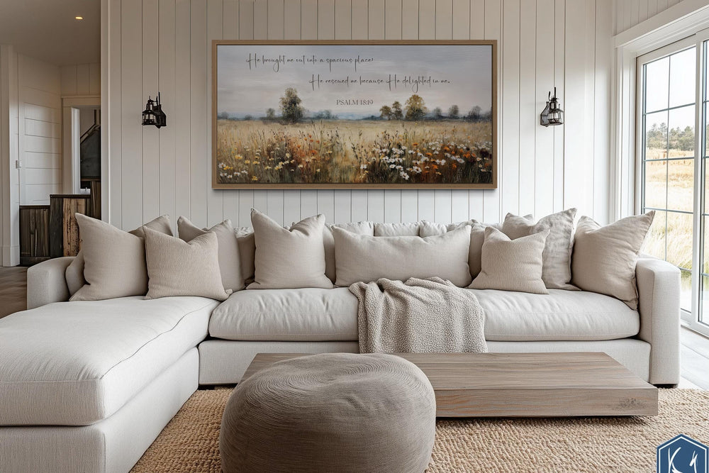 Psalm 18:19 scripture wall art on a wildflower field canvas above a neutral sectional sofa.