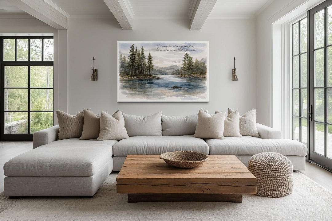 A serene lake landscape canvas print with Psalm 18:19 scripture hangs above a modern neutral sofa.