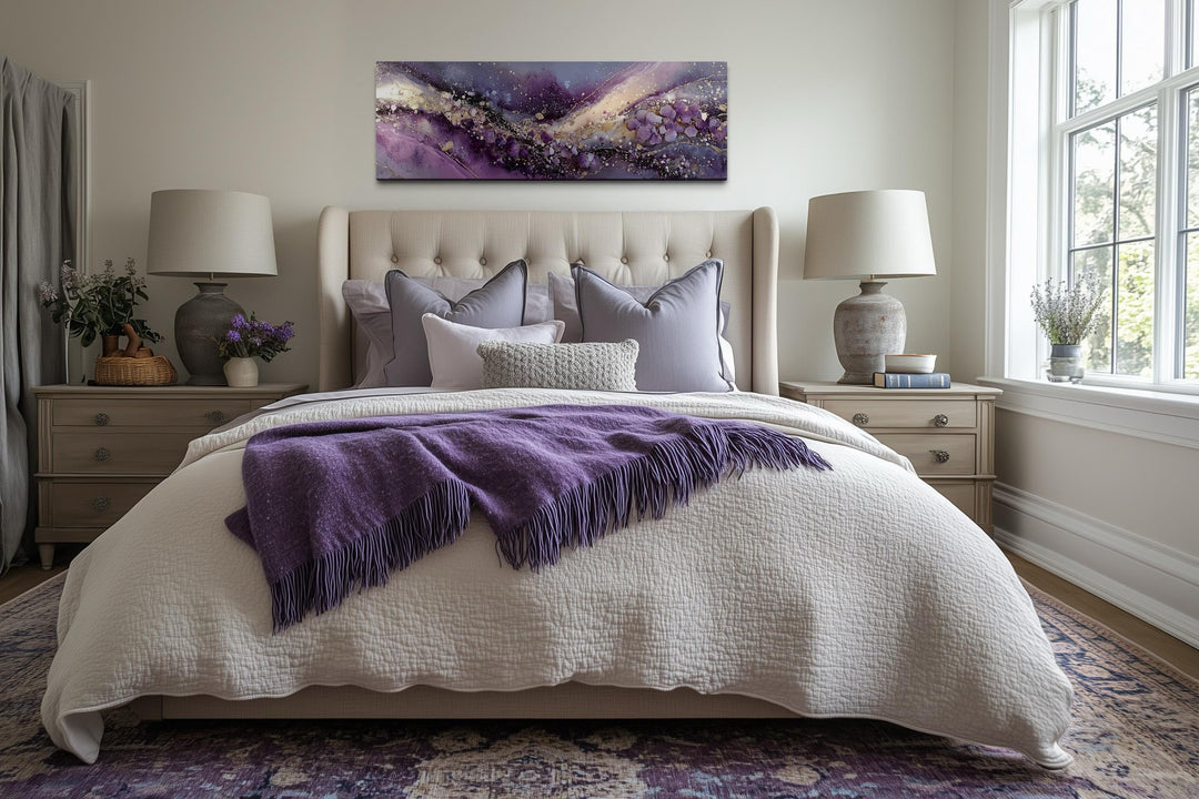 Purple abstract landscape canvas print with gold accents hanging above a neutral tufted bed.