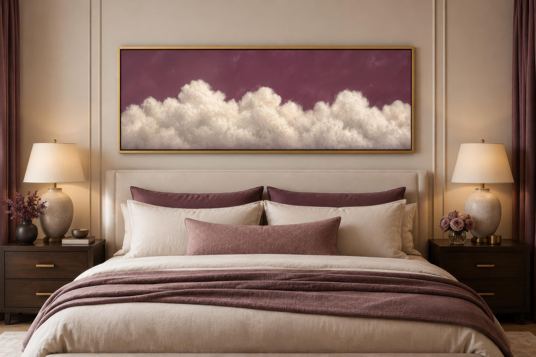 Long narrow canvas print of white fluffy clouds on a deep purple background above a bed.