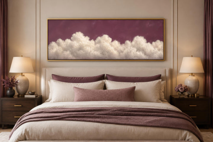 Long narrow canvas print of white fluffy clouds on a deep purple background above a bed.
