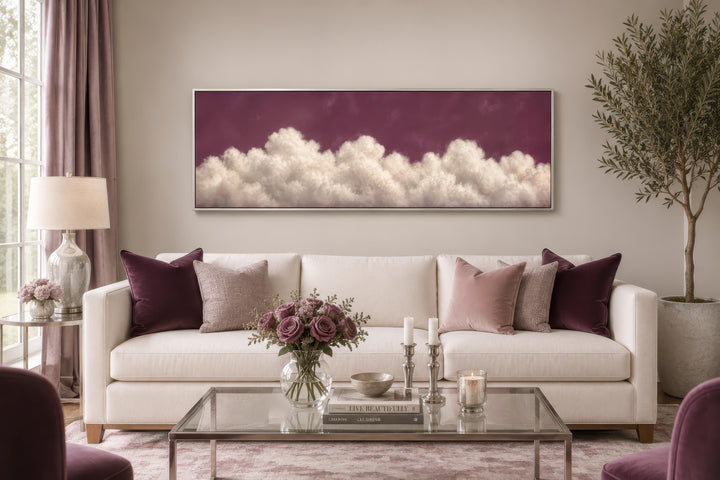 Long narrow canvas print of white fluffy clouds against a deep purple background above a sofa.