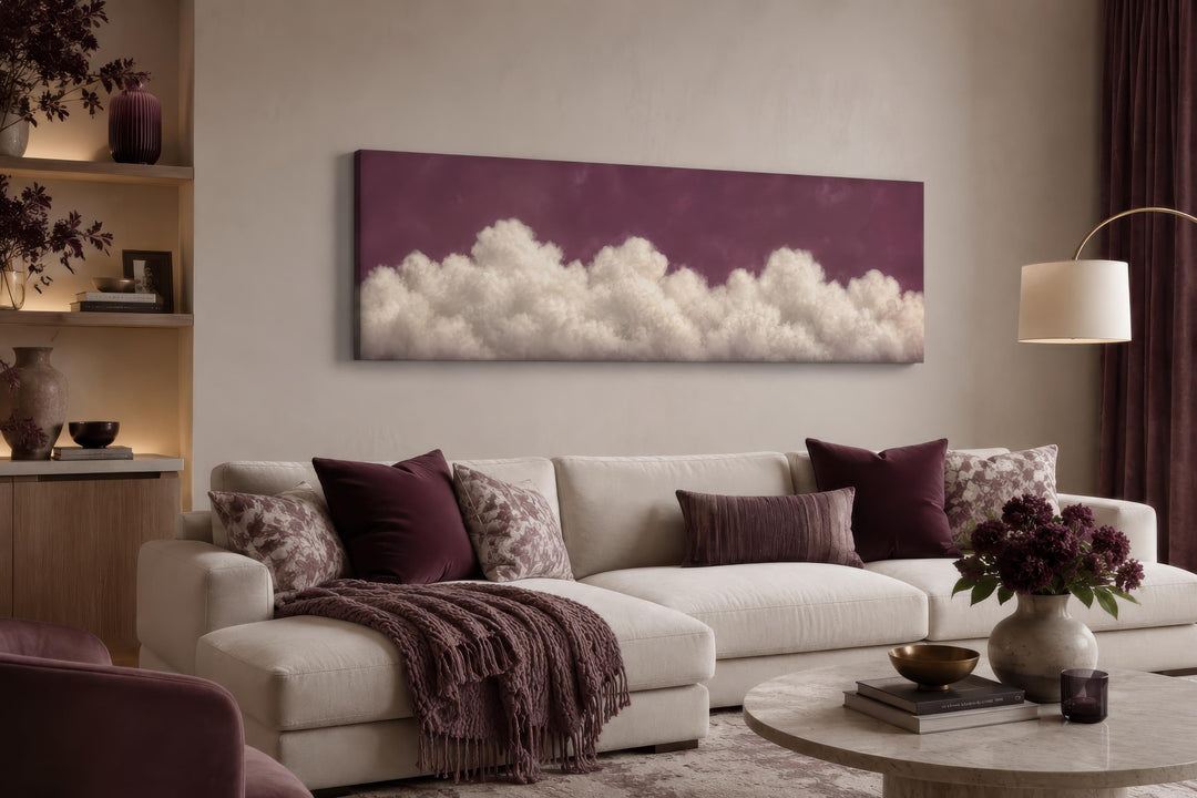 Long narrow canvas print of white fluffy clouds against a deep purple background above a sofa.