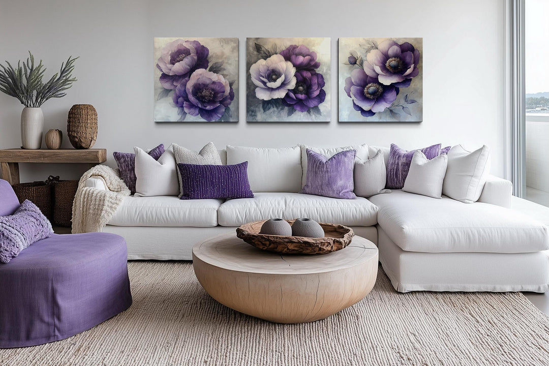 Set of three purple floral canvas prints hanging above a white sofa in a modern living room.