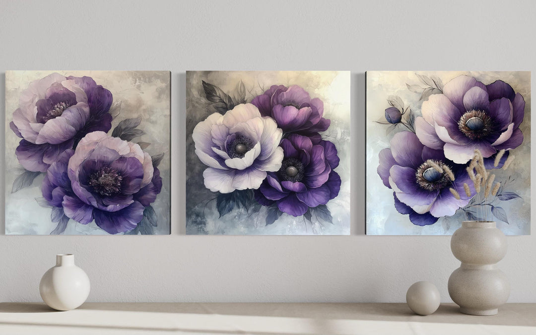 Set of three purple floral canvas prints displayed on a wall above a console with neutral vases.