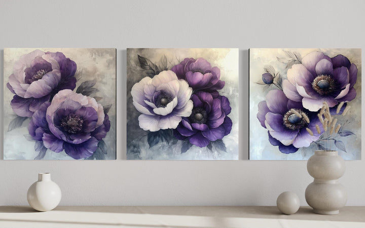 Set of three purple floral canvas prints displayed on a wall above a console with neutral vases.