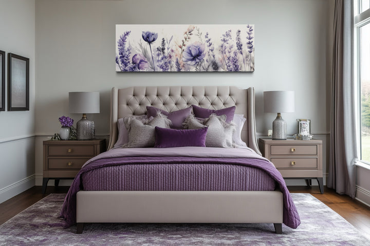 Panoramic framed canvas wall art of purple lavender wildflowers hanging above a tufted bed.