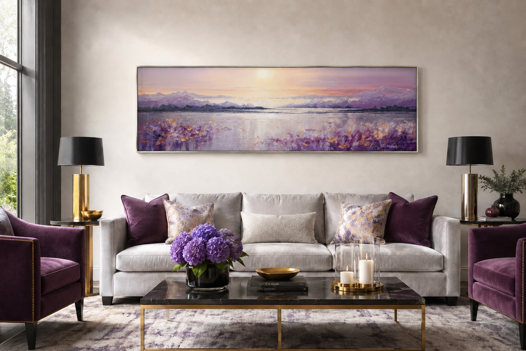 Long horizontal painting of a purple mountain lake sunset hanging above a grey sofa.