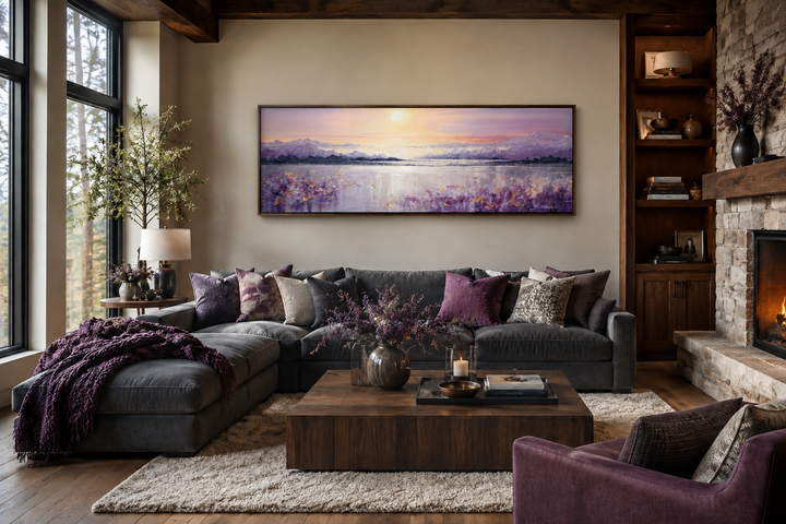 Long horizontal painting of a purple mountain lake sunset hanging above a dark grey sectional sofa.