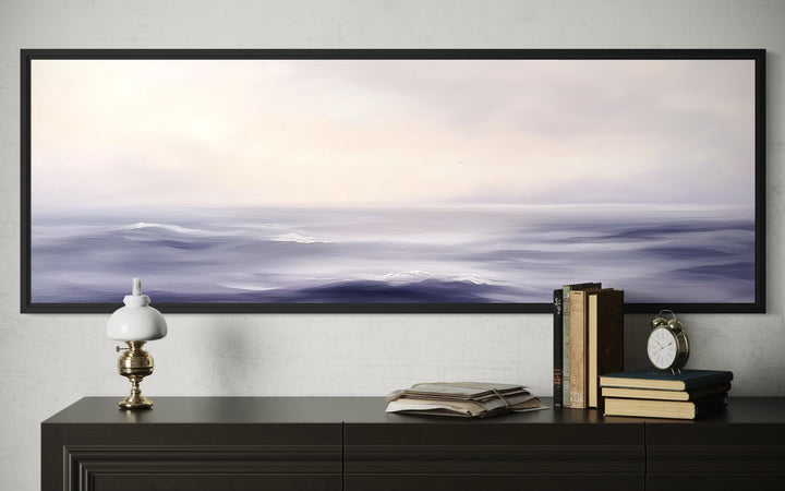 Purple Ocean Waves long horizontal coastal canvas wall art in a black frame above a dark sideboard.