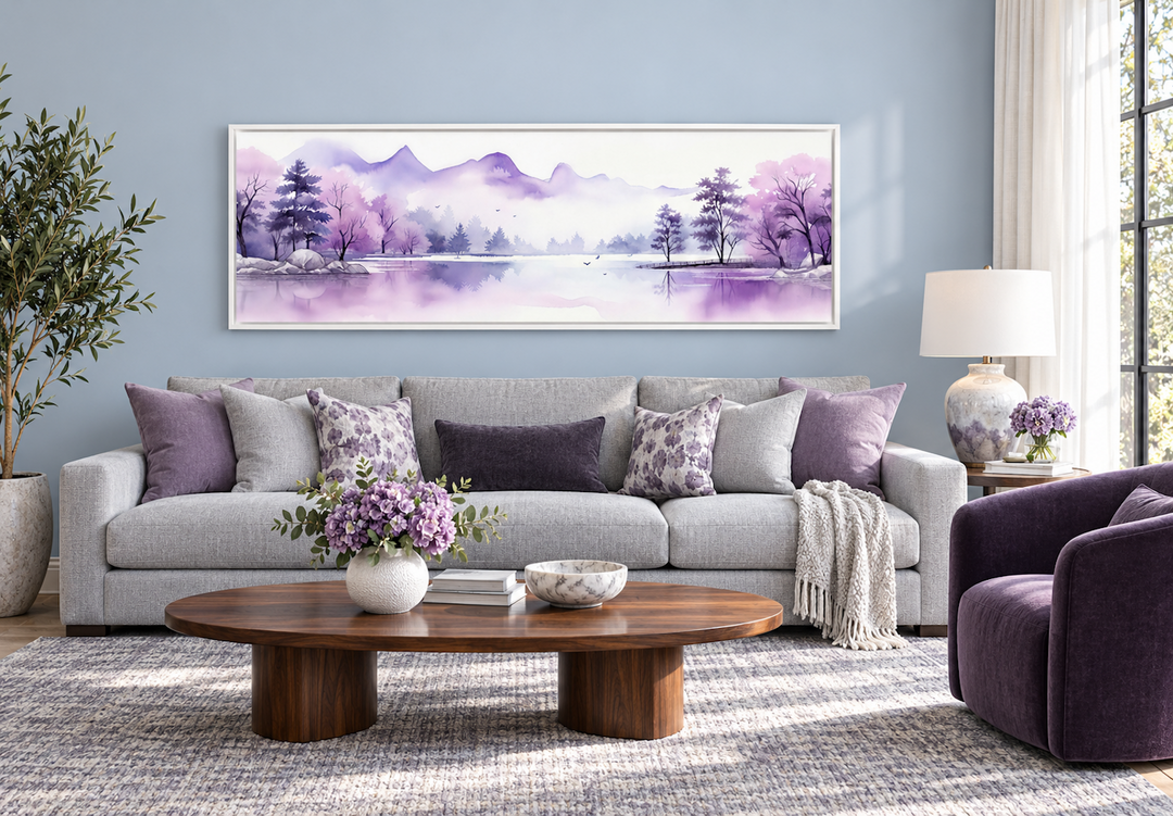 Long horizontal watercolor wall art of purple mountains and a lake above a gray sofa.