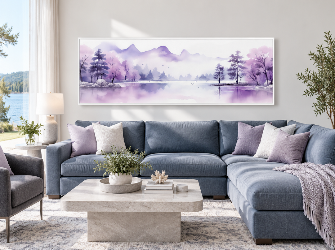 Long horizontal watercolor wall art of purple mountains and a lake above a blue sectional sofa.