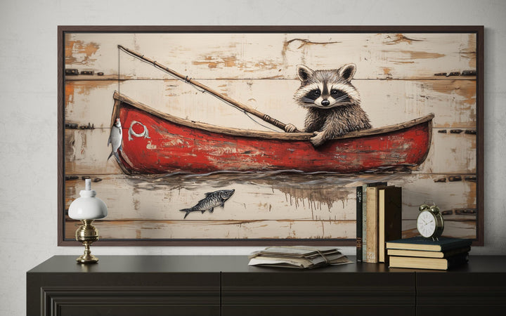 Whimsical raccoon fishing wall art in a red canoe on a rustic wood-style background.