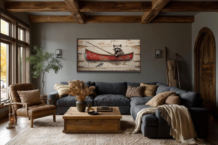 Whimsical wall art of a raccoon in a red canoe fishing, displayed in a rustic living room.