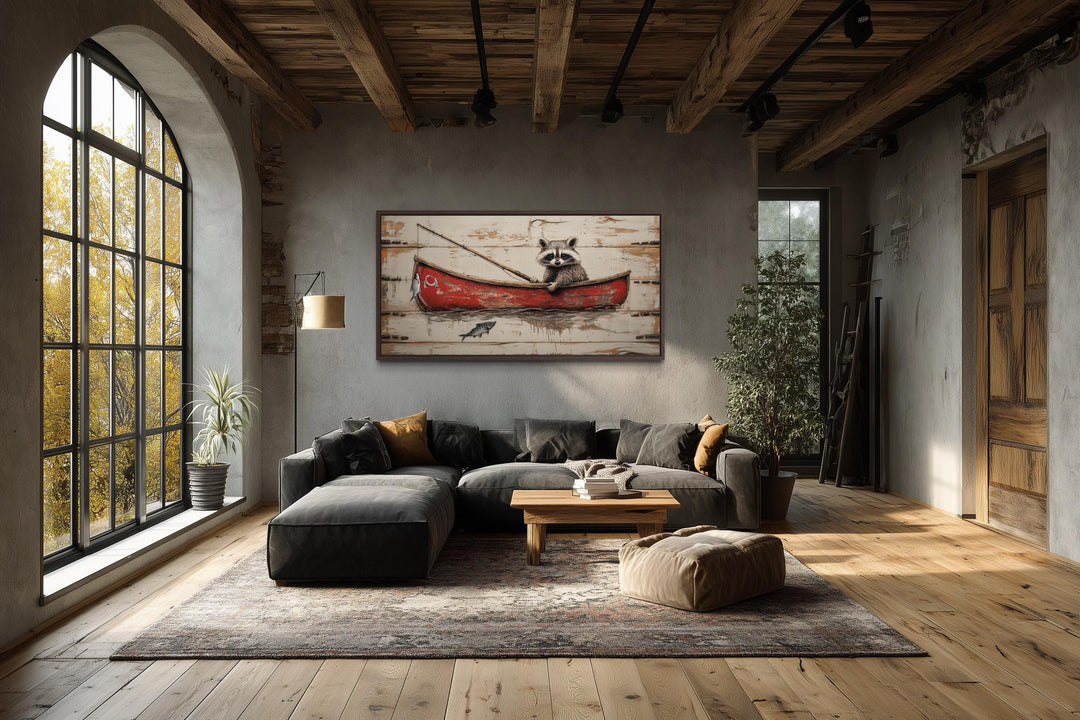 Whimsical wall art of a raccoon in a red canoe fishing, displayed in a rustic living room.