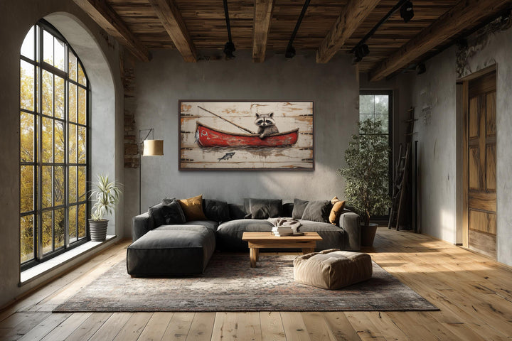 Whimsical wall art of a raccoon in a red canoe fishing, displayed in a rustic living room.