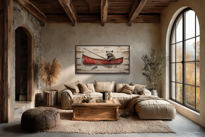 Horizontal wall art of a raccoon fishing in a red boat hangs in a rustic, cozy living room.