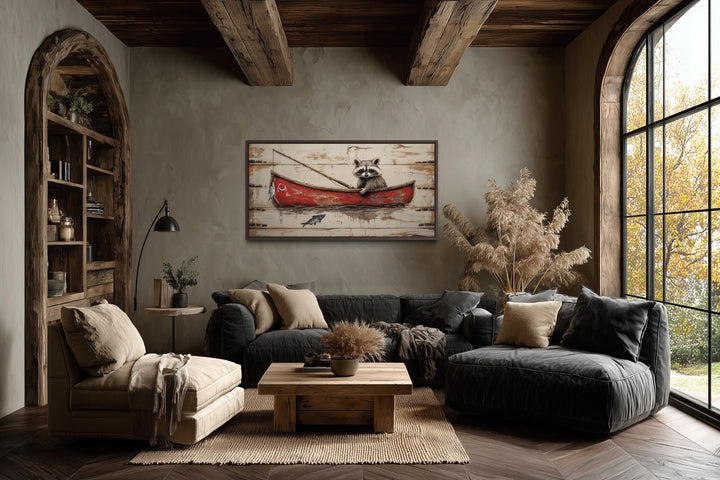 Whimsical wall art of a raccoon fishing in a red canoe, displayed in a rustic living room.