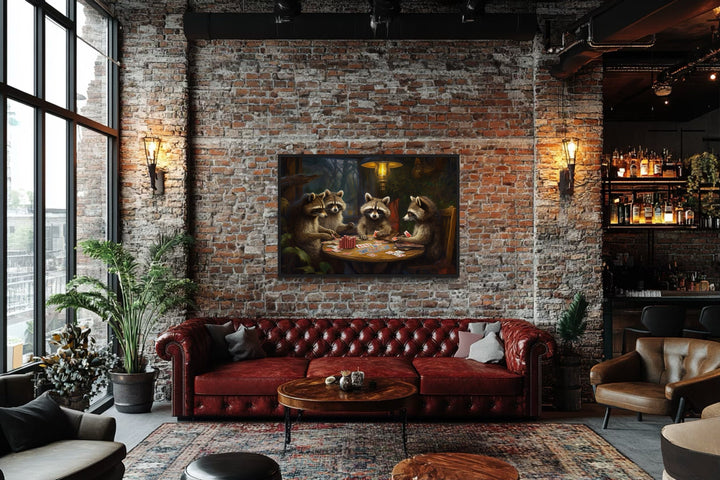 Raccoons playing poker framed canvas wall art hanging on a brick wall above a red leather sofa.