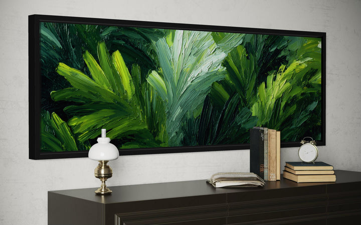 Panoramic rainforest jungle leaves canvas print in a black frame above a dark wood dresser.