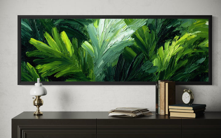 Horizontal canvas print of textured green jungle leaves in a black frame above a dark sideboard.