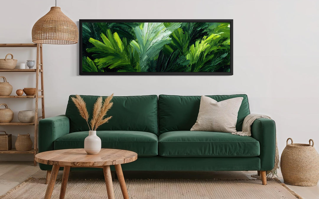 A long horizontal canvas print of lush green rainforest leaves hangs above a green velvet sofa.
