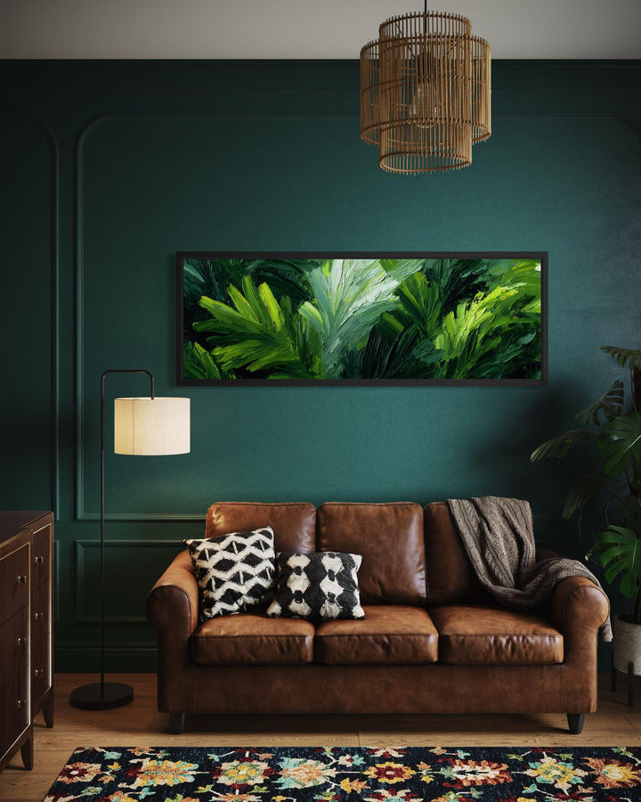 A long horizontal canvas print of lush green rainforest leaves hangs above a brown leather sofa.