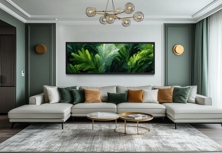 A long horizontal canvas print of lush green tropical leaves hangs above a modern gray sofa.