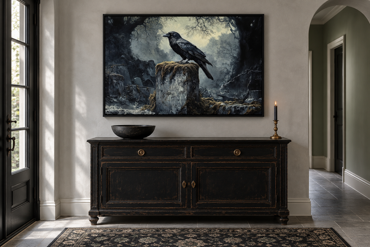 Framed gothic wall art of a black raven on a tombstone in a cemetery above a black sideboard.