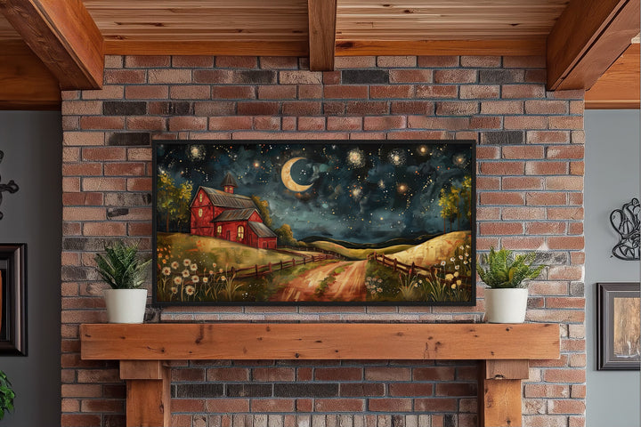 Framed wall art of a red barn under a crescent moon and starry night sky above a wooden mantel.