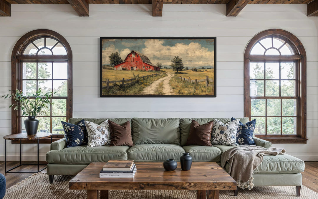 Large horizontal canvas print of a red barn in a rustic landscape above a green sofa.