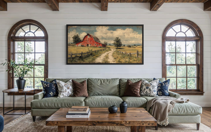 Large horizontal canvas print of a red barn in a rustic landscape above a green sofa.