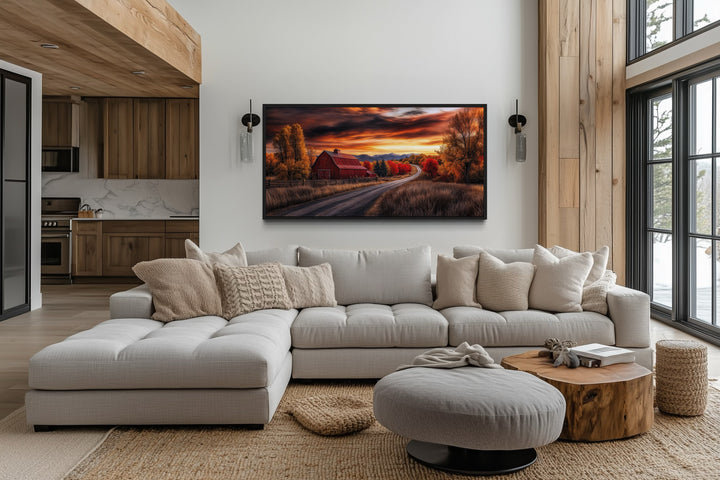 Red barn wall art in a rustic fall landscape hanging above a modern sectional sofa in a living room.