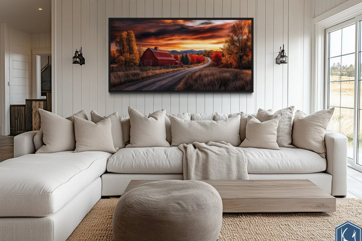 Red barn wall art in a rustic fall landscape, framed and hanging above a cozy farmhouse sofa.