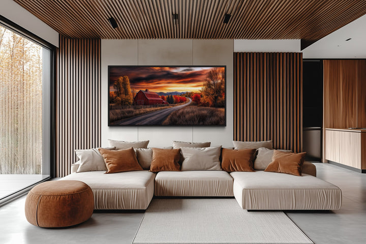 Red barn wall art in a rustic fall landscape, framed and hanging above a modern sectional sofa.