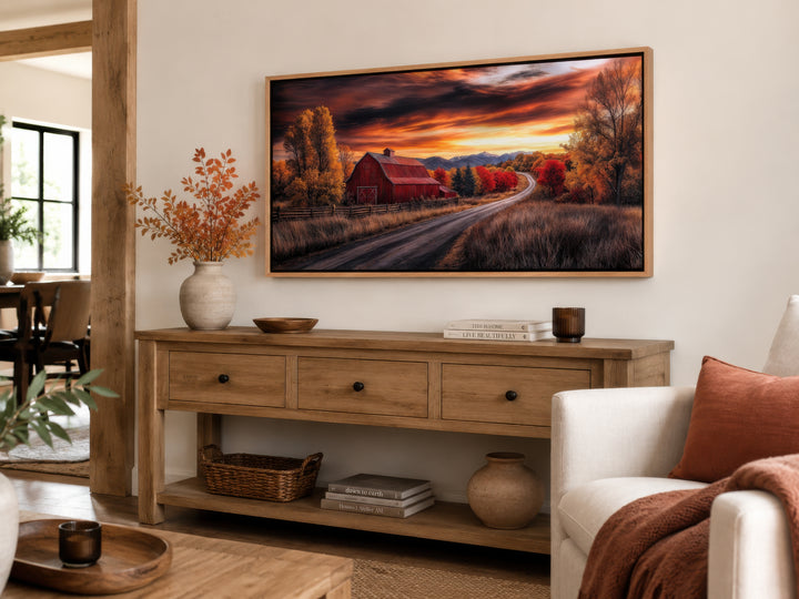 Framed red barn wall art with fall foliage and sunset over a console table in a farmhouse living room