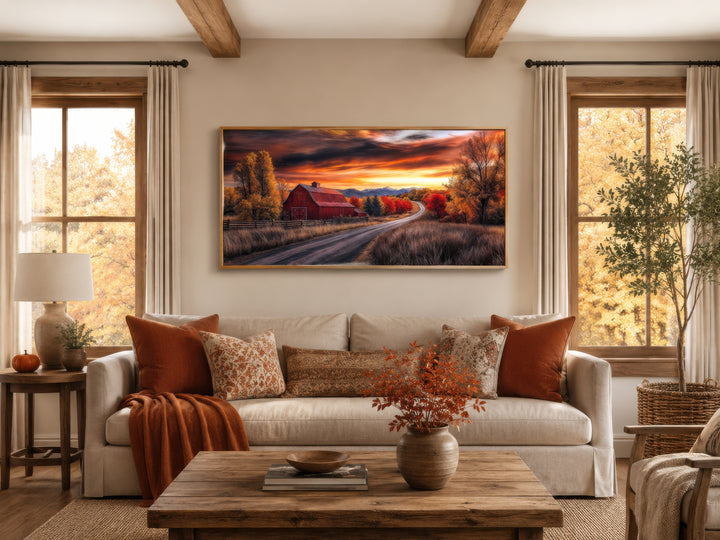 Red barn wall art in a rustic fall landscape hanging above a sofa in a cozy farmhouse living room.